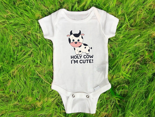 Cute white baby onesie featuring a unique sublimated design of an adorable cartoon cow with the playful phrase “Holy Cow I’m Cute!”—perfect for parents shopping funny baby clothes, newborn baby shower gifts, or gender-neutral infant outfits. The original farm animal design was hand-drawn by the shop owner and applied using high-quality printable vinyl for vibrant, long-lasting color. Ideal for baby milestone photos, everyday wear, or gifting a newborn with a personalized and handmade touch that can’t be fou