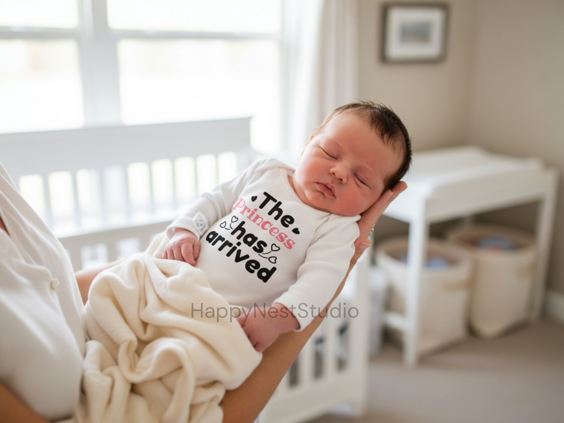 White long-sleeve baby girl onesie featuring a unique sublimated design that reads ‘The Princess Has Arrived’ in black and soft pink lettering with adorable heart accents. This handmade infant onesie is perfect as a birth announcement outfit, newborn photo shoot clothing, or a thoughtful gift for new parents welcoming their baby girl. Ideal for shoppers searching for cute baby girl onesies, princess newborn outfits, royal baby announcement bodysuits, unique sublimation baby clothes.